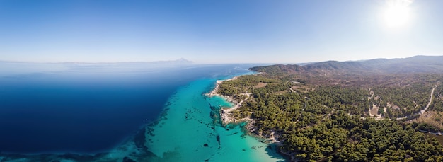 Wide shot of the Aegean sea coast with blue transparent water, greenery around, pamorama view from the drone, Greece