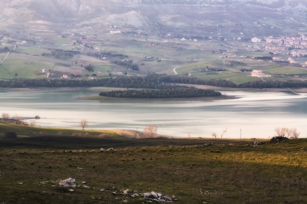 Wide shot of the beautiful sea surrounded by green trees and buildings covered in fog