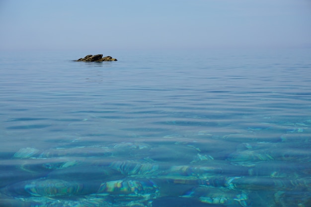 Free photo wide shot of a calm ocean  with a rock formation far from the shore