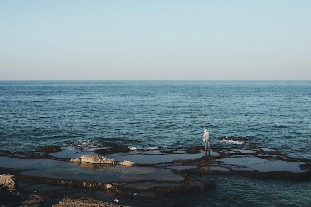 Wide shot of a fisherman standing on the shore during daytime