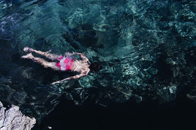 Wide shot of a person wearing pink and white swimsuit swimming in a clear sea