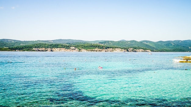 Free photo wide shot of a sea with buildings on the shore and forested mountains in the distance