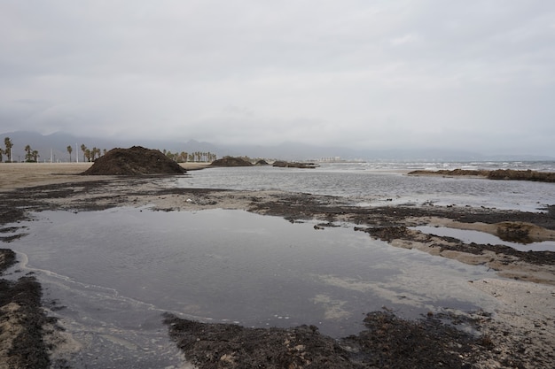 Wide shot of a seashore with a pile of black sand