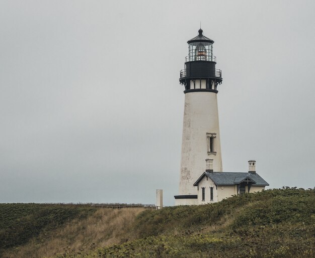 Wide shot of a white and black lighthouse near a house on the top of a hill