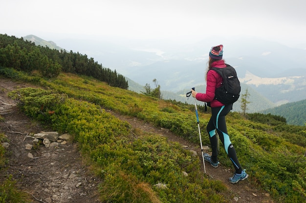 Free photo wide shot of a woman walking up a mountain with complete gear on a cold and foggy weather