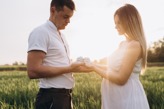 The wife and husband  keeping babyish shoes and standing on the field