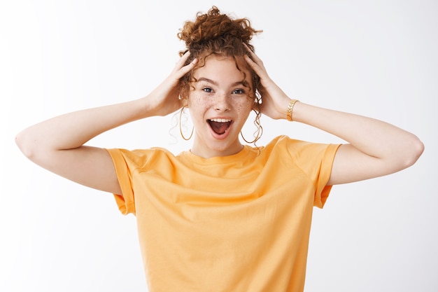 Free photo wild emotive energized good-looking young 20s redhead girl messy curly hairbun wearing orange t-shrit shouting amused having fun standing joyful mood touching head thrilled, white background