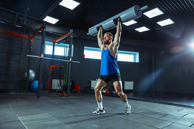 Wild energy. Young muscular caucasian athlete training in gym, doing strength exercises, practicing, work on his upper body with weights and barbells. Fitness, wellness, healthy lifestyle concept.