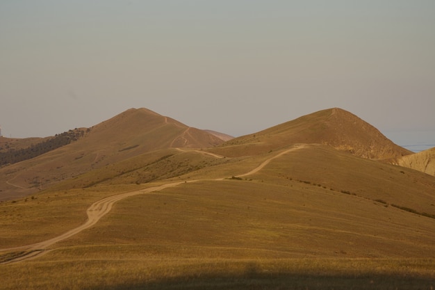 Wilderness, desert, landscapes, outdoors and wild nature concept. Country road running across deserted area between two high hills. Dry brown highlands with blue sea showing up in background