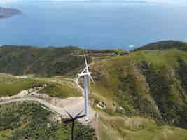 Free photo wind turbine generating power on a green wind farm with a beautiful sea view