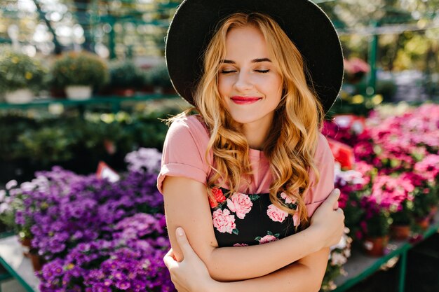 Winderful woman smiling with eyes closed on orangery. Beautiful romantic woman standing in frint of flowers.