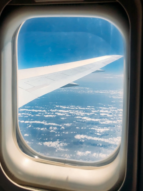 Wing through the window of airplane in amazing sky at sunset