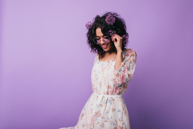 Free photo winsome african girl posing in dress with floral pattern. portrait of carefree black lady with alliums in hair.