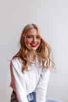 Free photo winsome blonde girl in shirt with smile.  happy caucasian lady isolated on light wall.