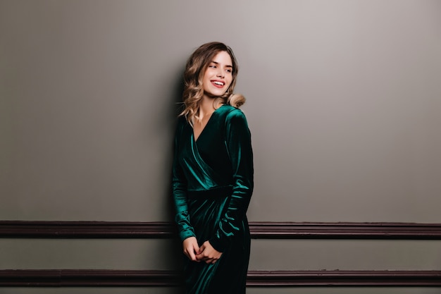 Winsome girl with elegant hairstyle preparing for party. Indoor portrait of stunning woman in long velvet dress.