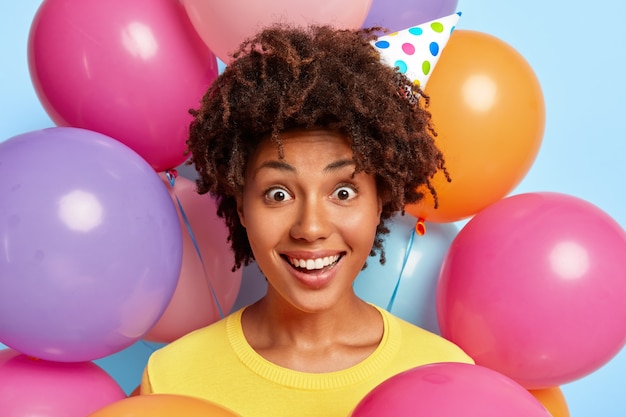 Winsome young woman posing surrounded by birthday colorful balloons