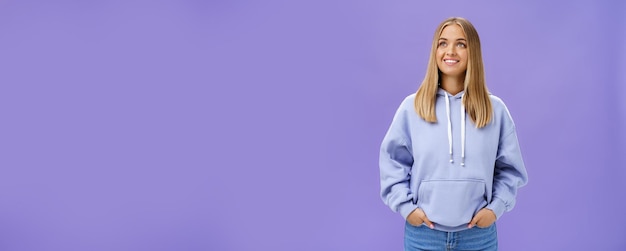 Free Photo winter comming dreamy kind and cute young girl with straight fair hair and tan wearing hoodie looking at upper left corner with nice white smile and admiring expression holding hand in pockets