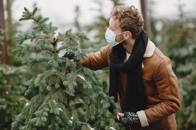 Winter concept. Guy in a brown coat. Salesman of Christmas Tree. Coronavirus theme.