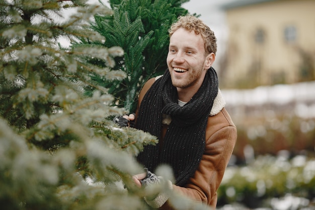 Free photo winter concept. guy in a brown coat. salesman of christmas tree.