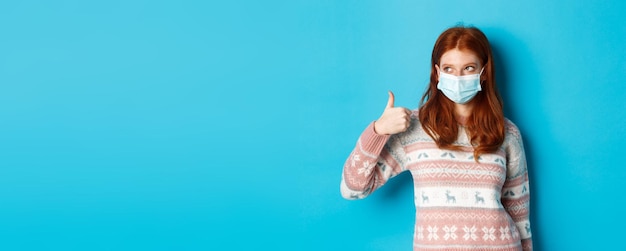 Free Photo winter coronavirus and social distancing concept pretty redhead girl in face mask and sweater lookin