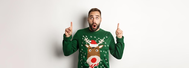 Free photo winter holidays and christmas amazed handsome man in new year sweater pointing fingers up showing lo