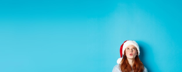 Free Photo winter holidays and christmas eve concept head of pretty redhead girl in santa hat appear from botto