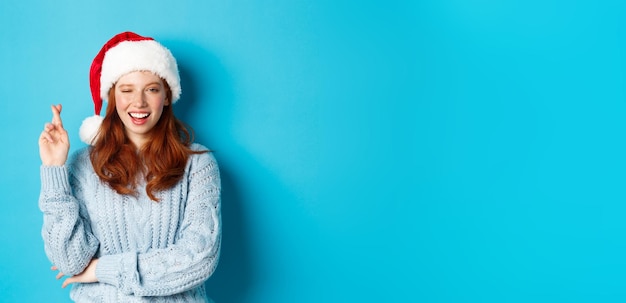 Free Photo winter holidays and christmas eve concept hopeful redhead girl in santa hat making wish on xmas cros