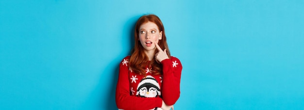 Free Photo winter holidays and christmas eve concept pretty redhead girl in xmas sweater touching cheek thought