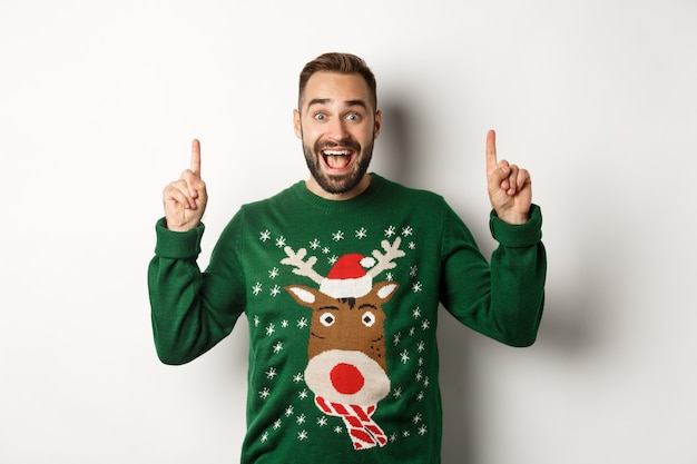 Winter holidays and christmas. Excited man pointing fingers up, showing advertisement, standing over white background