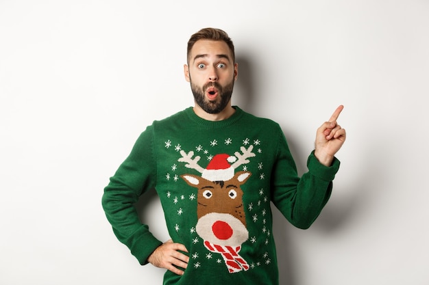 Winter holidays and christmas. Man looking excited as pointing finger right at logo, standing amazed against white background