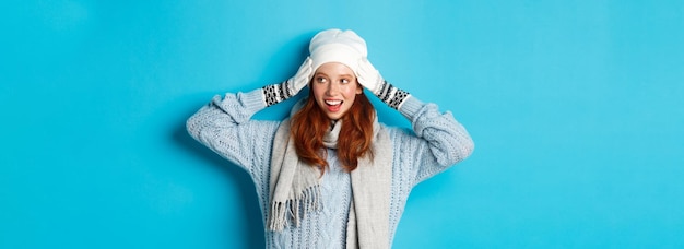 Free photo winter and holidays concept happy redhead girl in beanie hat scarf and gloves looking right and smil