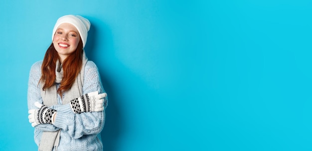 Free photo winter and holidays concept smiling redhead girl in beanie gloves and sweater getting warm after goi