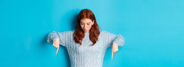 Free Photo winter holidays and people concept intrigued redhead girl pointing and looking down thoughtful makin