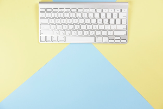 Free photo wireless white keyboard on yellow and blue background