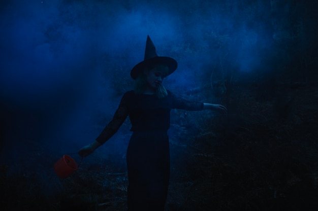 Witch girl with bucket in night forest 