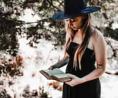 Free photo witch in hat reading aged book in forest daytime