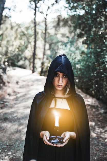 Free photo witch in hood with candle in woods