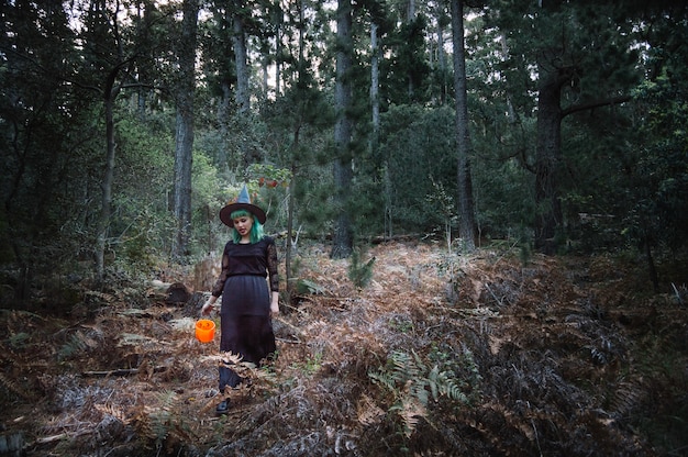 Witch with bucket walking in forest