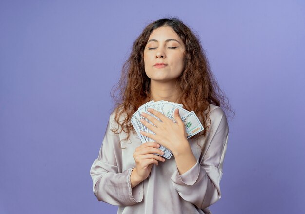 With closed eyes impressed young pretty girl holding money isolated on blue wall