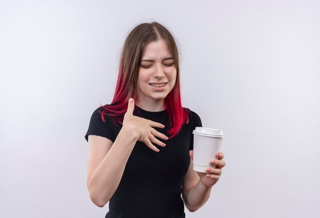 With closed eyes young beautiful girl wearing black t-shirt holding cup of coffee on isolated white wall