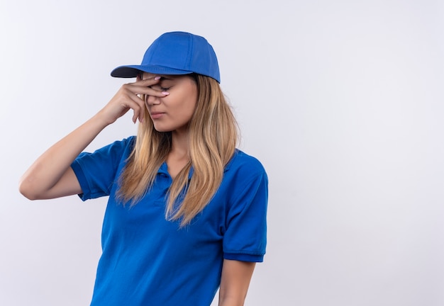 Free photo with closed eyes young delivery girl wearing blue uniform and cap putting hand on eyes isolated on white wall with copy space