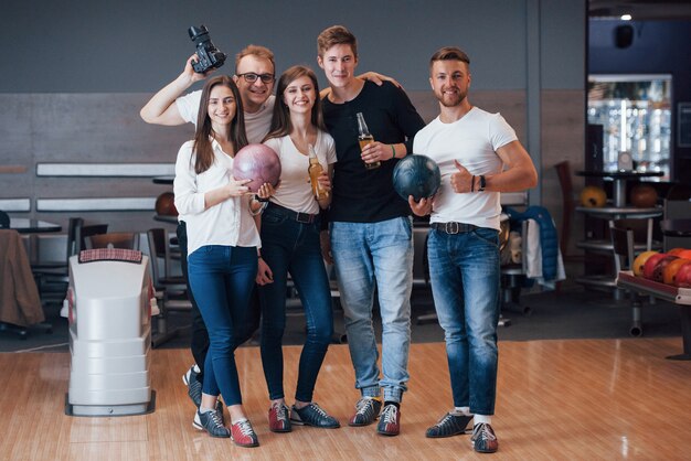 With photographer. Young cheerful friends have fun in bowling club at their weekends