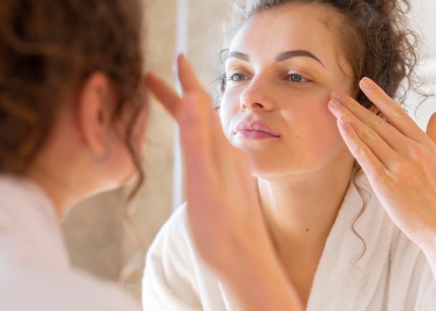 Woman applying cream on face while looking in mirror