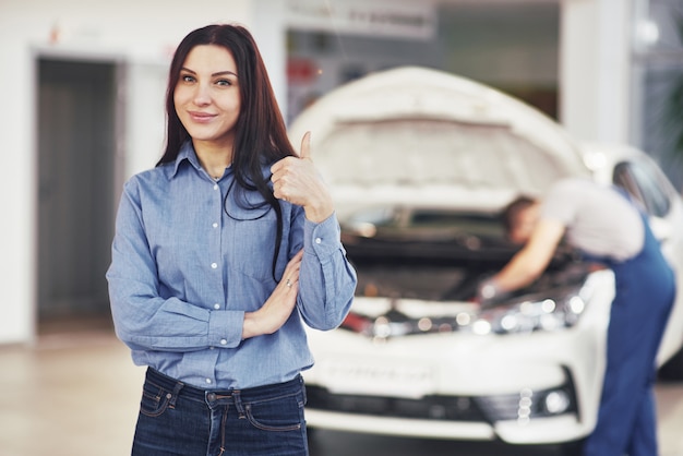 The woman approves the work done by the client. The mechanic works under the hood of the car