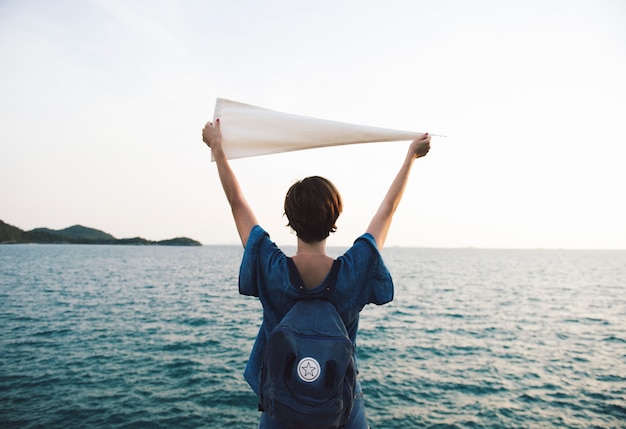 Free photo woman arms raised and holding flag by the sea in rear view