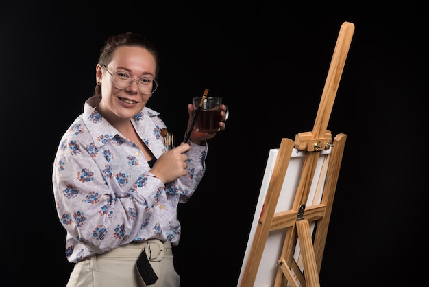 Woman artist holding brush and canvas on black background . 