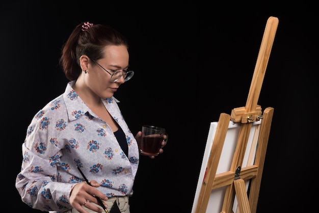 Woman artist holding brush and looking at canvas on black