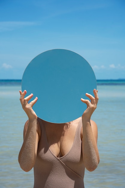 Woman at the beach in summer posing with round mirror