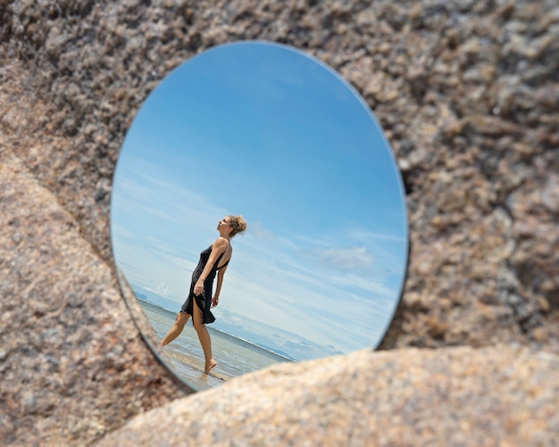 Free Photo woman at the beach in summer posing with round mirror