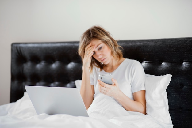 Free Photo woman in bed using laptop and mobile